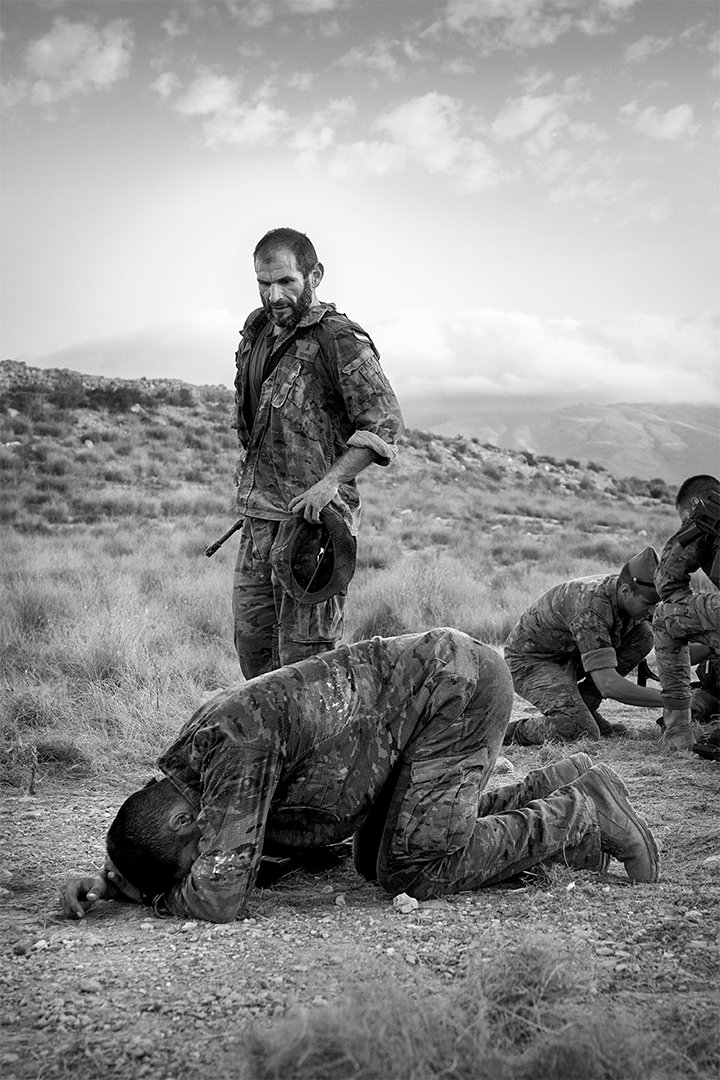A service member standing beside others lying on the ground.